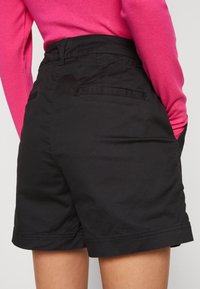 Černé šortky s rovnýcm střihem, s plochým pasem a dvěma zadními kapsami. Navrženy z hladkého, lehkého materiálu.