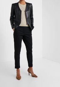 Giacca di pelle nera con un design aderente, maglione beige sotto, pantaloni neri tagliati su misura e tacchi alti a righe marroni.