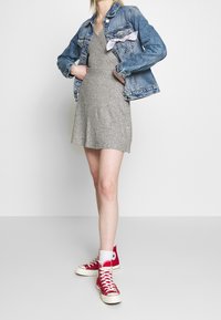 Šedé pletené šaty se zvonovým lemem, vrstvené pod modrou denimovou bundou s růžovou mašlí. Kombinované s červenými vysokými teniskami.