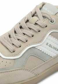 Beige suede sneaker with textured gray accents, white side stripe, and woven beige laces. Features perforations on upper for ventilation.
