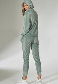 Velvet jogging set in een zachte groene kleur. Hoodie met lange mouwen en zijzakken. Tapered broek met elastische cuffs. Witte sneakers.