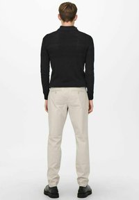 Pull noir en tricot avec un col montant, accompagné de pantalons beige clair, dotés d'une finition lisse et d'un design simple, vu de dos.
