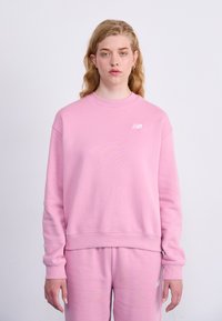 Sweat-shirt rose clair avec un col rond et des poignets côtelés, arborant un petit logo blanc sur la poitrine gauche et une coupe décontractée.