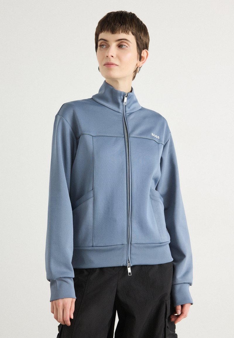 Blue zip-up sweatshirt made of soft fabric, featuring a high collar, two side pockets, and a subtle logo on the chest. Smooth texture.