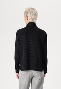 Svart långärmad skjorta med ett subtilt diagonalt randmönster, mjuk textur och hög krage. Fodrade manschetter fullbordar den sofistikerade designen.