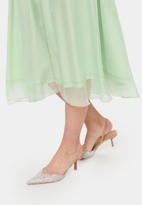 Tűsarkú slingback cipők hegyes orral, ezüst strasszokkal díszítve. Az alap bézs színű, az pánt pedig vékony és átlátszó.