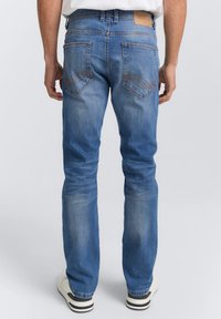 Vaqueros de denim azul con corte recto, que presentan bolsillos traseros y una etiqueta de cuero marrón en la cintura. Textura suave, lavado claro.