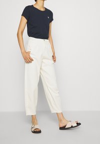 Navy short-sleeve t-shirt with a small logo, paired with white high-waisted pants and light pink sandals featuring a decorative strap.
