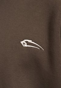 Braunes Baumwollkleidungsstück mit gerippter Textur, auf der oberen linken Seite mit einem weißen gestickten Logo ausgestattet.