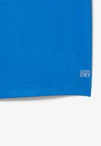 Sininen aktiiviliikuntapaita, jossa on sileä tekstuuri ja helman etiketti, jossa lukee "ULTRA DRY". Suunnittelu korostaa toiminnallisuutta ja kosteudensääntöä.