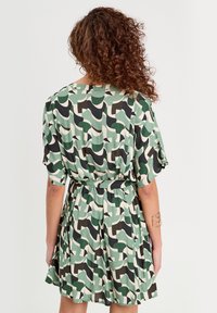Robe à manches courtes présentant un motif abstrait vert, noir et crème, avec une taille ceinturée et une jupe fluide. Tissu doux, coupe décontractée.