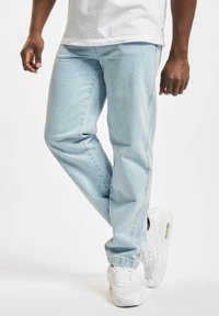Light blue denim jeans with a relaxed fit, featuring visible stitching, and a straight leg design. Paired with white sneakers.