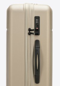 Twarda walizka w metaliczno-beżowym kolorze, z teksturowaną powierzchnią, czarnym uchwytem bocznym i zamkiem szyfrowym dla bezpieczeństwa.