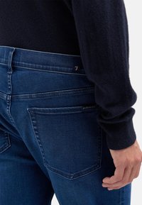 Ciemnoniebieskie jeansy z denimu o dopasowanym kroju, z kontrastowym przeszyciem, dwoma tylnymi kieszeniami i subtelną metką z logo na pasku talii.