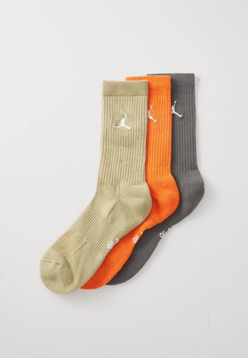 Tres pares de calcetines de canalé en verde oliva, naranja brillante y gris oscuro, cada uno con un logo blanco en el puño.