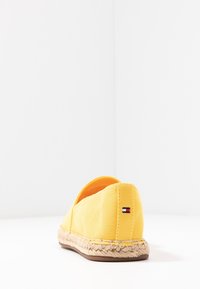 Espadrille en toile jaune avec une semelle en jute tissée, présentant des accents cousus et un petit logo sur le talon.