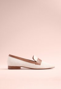 Mocassins en toile crème avec une bande en cuir marron, bout pointu, petit talon en bois et texture lisse sur un fond rose doux.