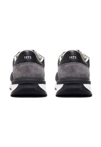 Graue und schwarze Sneakers aus Wildleder und Leder, mit einer weißen Sohle und schwarzem Außensohle, geprägt mit "1973" an der Ferse.