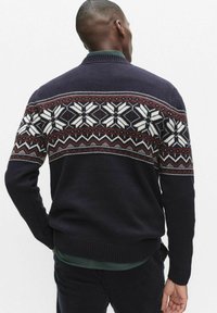 Granatowy sweter z wzorem dzianiny z białymi śnieżynkami i bordowymi akcentami. Sweter wykończony jest ściągaczami na mankietach i u dołu.