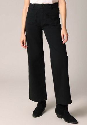 Zwarte wijde broek van katoen met hoge taille, voorzien van vo pockets en een gladde textuur. Draagt met zwarte enkellaarsjes met hak.
