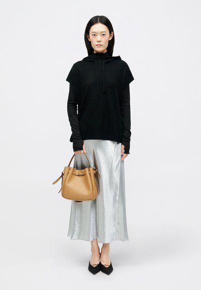 Μαύρη κοντομάνικη κουκούλα με κορδόνια, συνδυασμένη με ασημένια σατέν μακριά φούστα. Κρατάει μια καφέ δερμάτινη τσάντα bucket και φορά μαύρες μυτερές γόβες.