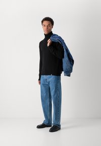 Μαύρος μπούφος, χαλαρού στυλ τζιν παντελόνι ανοιχτού μπλε, μαύρα παπούτσια και μια τζάκετ τζιν μπλε ριγμένο στον ώμο.