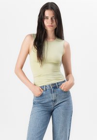 lichtgroene mouwloze top met een strakke pasvorm, gecombineerd met hoge, blauwe jeans in een klassieke vijf-pocket stijl.