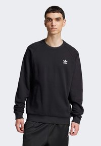 Felpa nera in cotone, con scollo a girocollo, maniche raglan lunghe e logo Adidas bianco sul petto. Texture liscia.