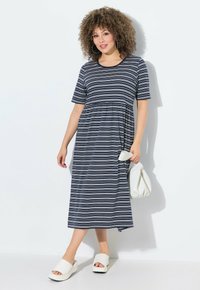 Niebieska sukienka w paski z krótkimi rękawami, zwiewną sylwetką i marszczonym pasem. Połączona z białymi sandałami na koturnie i białą torebką.