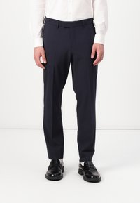 Pantalones de vestir azul marino, confeccionados en tela suave, con un diseño de pierna recta, trabillas para cinturón y pliegues frontales, combinados con mocasines negros.