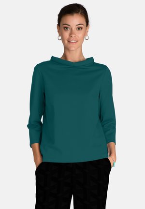 Teal, soft fabric top with a cowl neckline and three-quarter sleeves, paired with black patterned pants. Plain design with no visible hardware.
