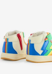 Šarena visokotopšna tenisica s kremastom podlogom, plavim akcentima, zelenim munjama, crvenim patentnim zatvaračima i dušicama duge na stranama.