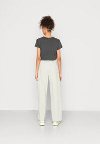 Gray short-sleeve t-shirt paired with light beige wide-leg pants and white sneakers with yellow accents, viewed from the back.