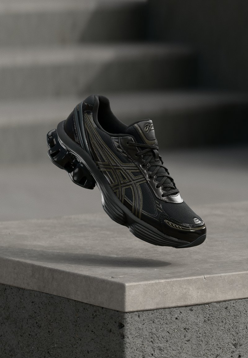 Sapatilha atlética preta com um upper de malha respirável, acabamentos brilhantes, um colarinho acolchoado e um design de sola distinta com mola.