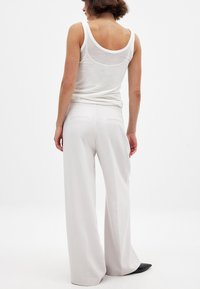 Laiad valged püksid, mis on valmistatud siledast kangast, keskmise kõrge vöökohaga ja kahe tagataskuga, koos sobiva valge tanktopiga.