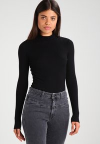 Top noir à manches longues côtelé avec un col montant, associé à un jean taille haute gris foncé avec une silhouette ajustée et des détails de couture subtils.