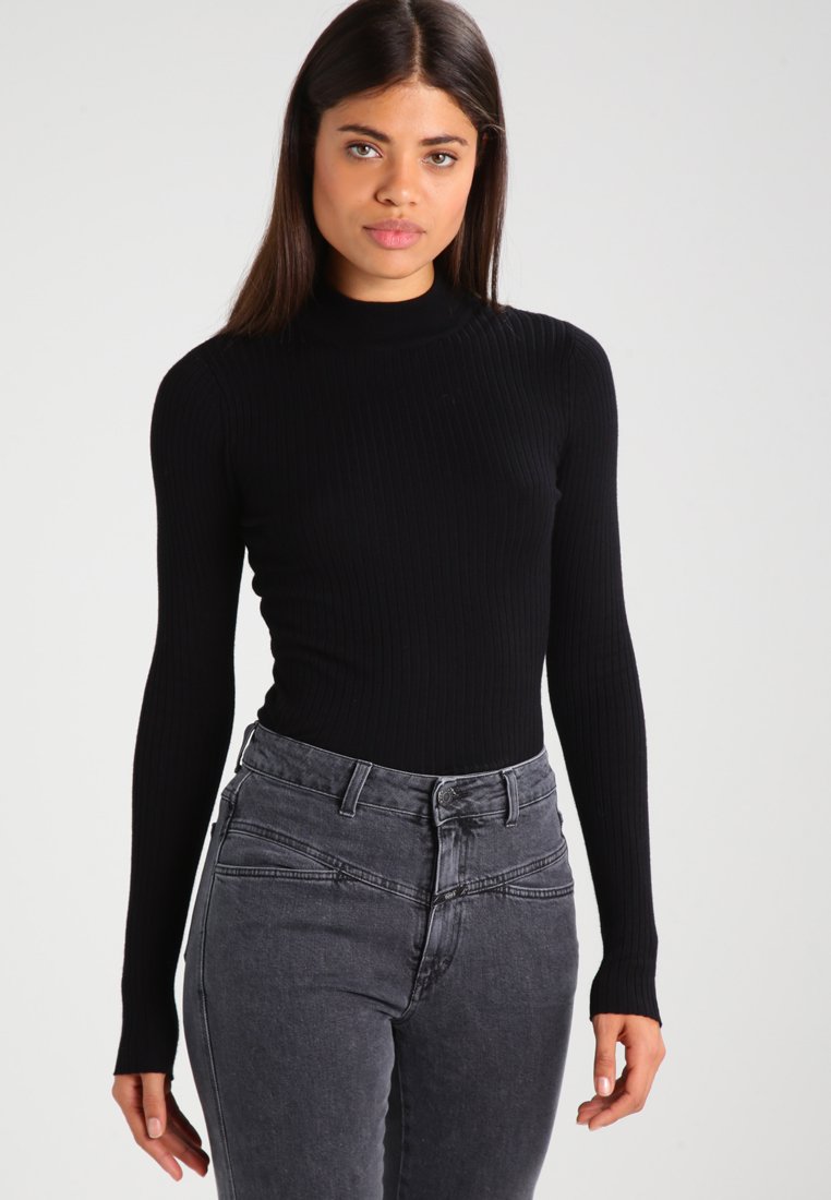 Top noir à manches longues côtelé avec un col montant, associé à un jean taille haute gris foncé avec une silhouette ajustée et des détails de couture subtils.