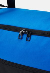Sac en tissu bleu avec une surface texturée, doté d'une fermeture éclair noire et de deux tirettes de fermeture sur le dessus. La section inférieure est noire.