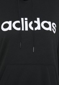 Felpa nera con cappuccio realizzata in tessuto morbido, con un grande logo bianco che recita "acildas". Presenta una tasca frontale e un cappuccio regolabile con coulisse.