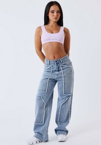 Top corto de canalé púrpura claro con un logo, combinado con jeans de mezclilla anchos azules con costuras blancas y parches desgastados. Zapatillas blancas.