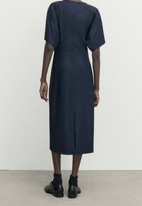 Navy Midi-Kleid aus strukturiertem Stoff, mit einem Schlitz hinten, kurzen Ärmeln und einem runden Ausschnitt, getragen mit schwarzen Schuhen und Socken.