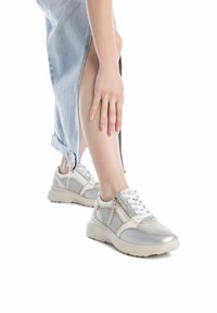 Zapatillas deportivas blancas y plateadas con detalles de malla, puntera redonda, suela gruesa y acentos de cremallera. Llevadas con una falda de mezclilla clara.