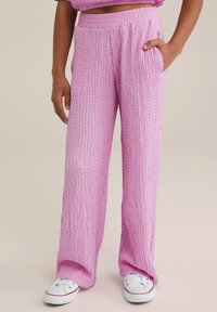 Svetlo rožnato, strukturirane hlače širokih nogavic z elastičnim pasom, ki imajo stranske žepke in sproščen kroj. V kombinaciji z belimi športnimi copati.