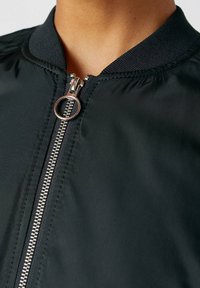 Černá bomber bunda s kulatým límcem, kovovým zipem a hladkým, mírně lesklým materiálem s jednoduchým designem.
