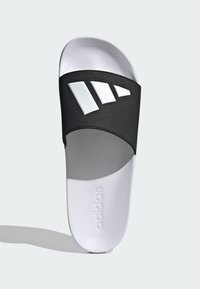 Black slip-on sandal with a textured strap featuring three white stripes. White footbed with embossed "adidas" logo. Smooth surface.