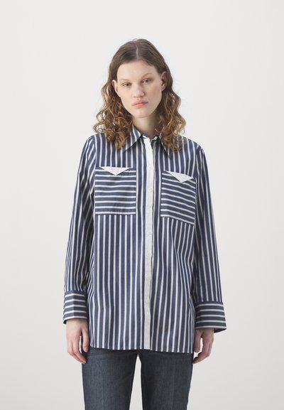 Camicia a righe con righe verticali blu navy e bianche, chiusura con bottoni sul davanti, due tasche sul petto e maniche lunghe con dettagli ai polsi. Tessuto in misto cotone.