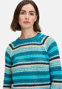 Pull en crochet avec des rayures horizontales turquoise, crème et marine, un col rond et une texture en maille légère et ouverte.