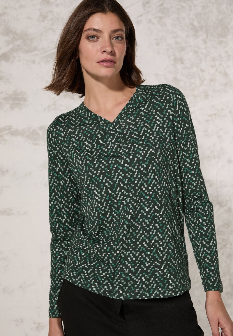 Langsleeve groene top met een geometrisch wit en teal patroon, voorzien van een V-hals ontwerp en een zachte textuur. Geschikt voor casual wear.