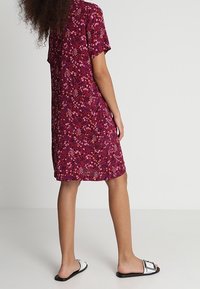 Kortærmet knælængde kjole i burgunder med blomsterprint. Letvægtsstof med en afslappet pasform, kombineret med flade sorte sandaler.
