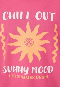 Roze katoenen T-shirt met een grote oranje zonafbeelding en golvende accenten. De tekst luidt "RELAX IN DE ZON" in wit en oranje.